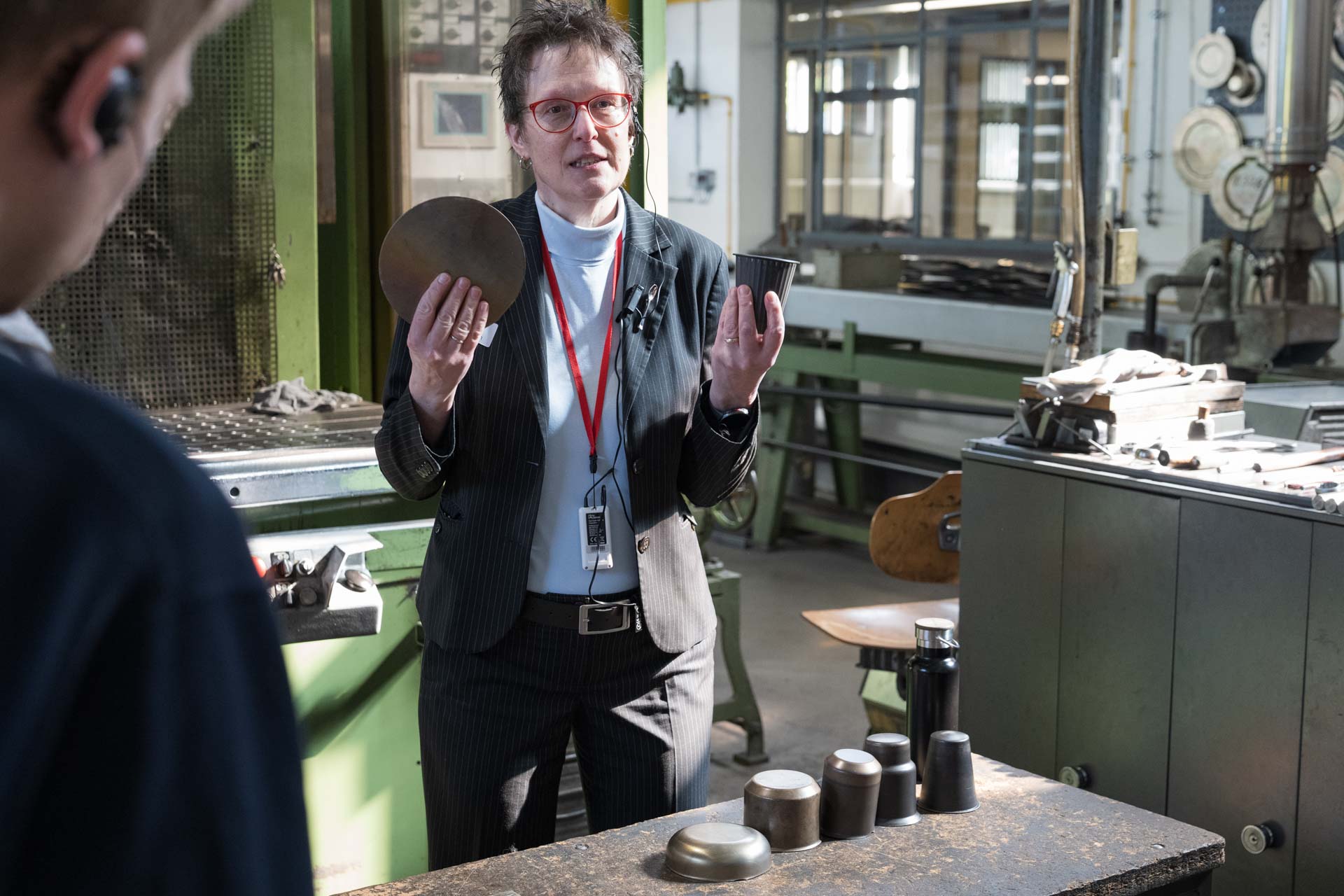 Eine Frau hält in einer Werkstatt zwei Metallgegenstände in den Händen